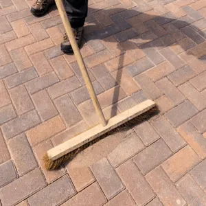 man veegt zand in voegen van terras