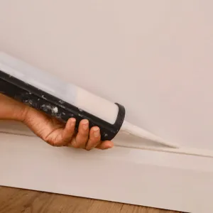 vrouw dicht kier van nieuwe plint met kitspuit