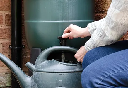 vrouw houdt gieter onder regenton